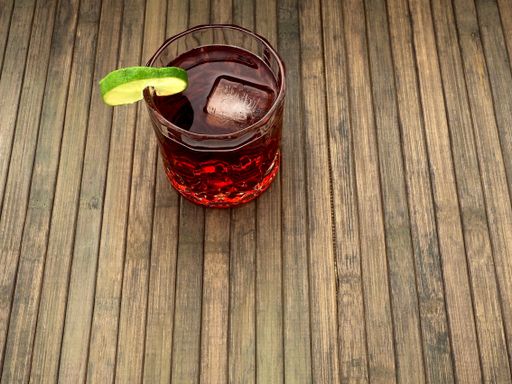 A closeup shot of a red cocktail with a slice of cucumber and ice cubes on the wooden background