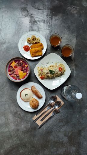 A top view of plates of pasta, dessert and a bottle of water on the table