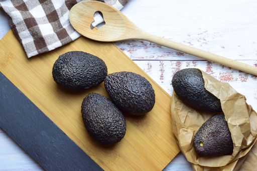 A top view of ripe avocados in a kraft paper bag and on a kitchen board on rustic white background