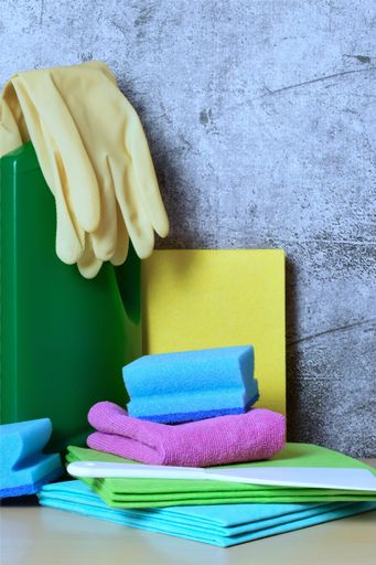 A vertical of household cleaning products such as sponges, gloves and detergent on a grunge background