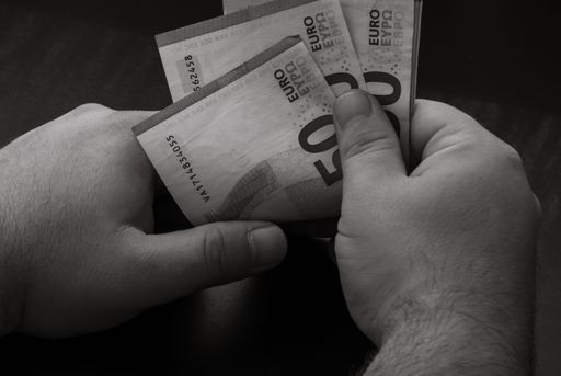 A grayscale closeup of person's hands holding and calculating stack of Euro banknotes