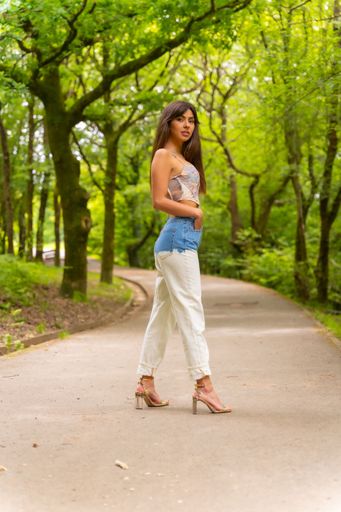 A beautiful Caucasian girl posing in jeans and a crop top in a city park path
