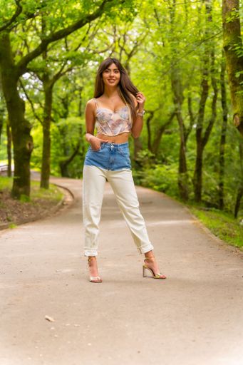 A beautiful smiling Caucasian girl posing wearing jeans and a crop top on a  city park path