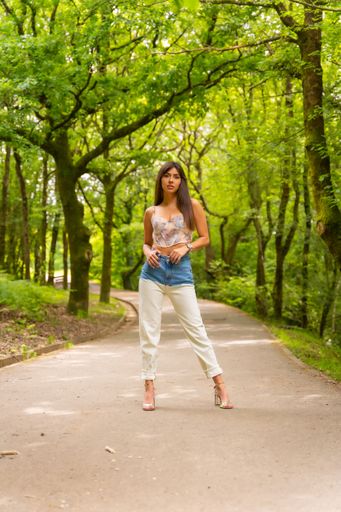 A beautiful Caucasian girl posing wearing jeans and a crop top on a  city park path