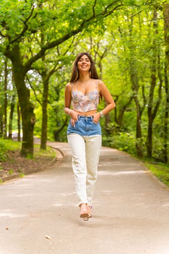 A beautiful smiling Caucasian girl posing wearing jeans and a crop top on a  city park path