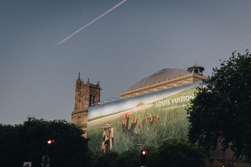 A big Louis Vuitton poster behind lush green trees during sunset