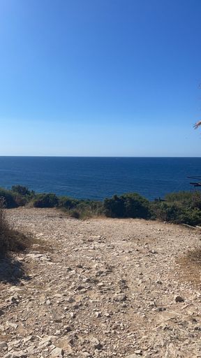 A vertical shot of a rocky ground with a sea in the background on a sunny day