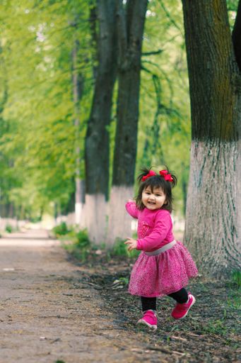 A close up of a little girl accompanied by her mother on a beautiful summer day walking through a small forest inside the city