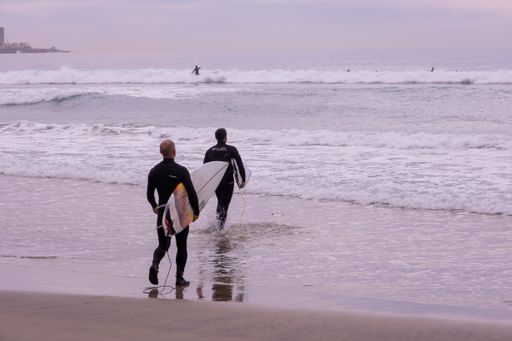 A rear view of male surfers carrying surfboards while walking on the beach