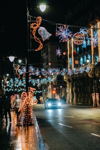 A vertical shot of a car driving on an empty street decorated with Christmas lights at night