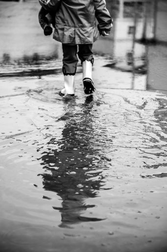 A grayscale shot of a child in rubber boots walking in water
