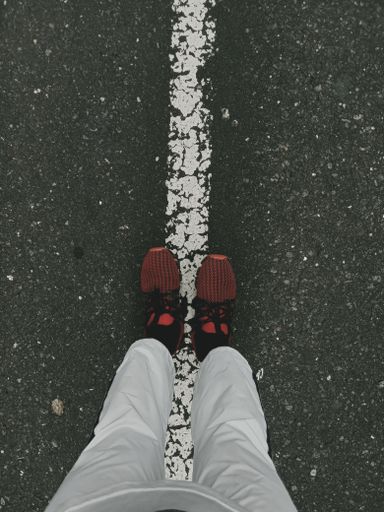 A vertical top view of a person with red running shoes standing on a white stripe on a road