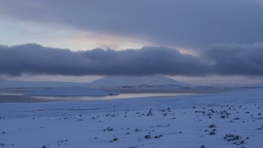 A wide shot of a snowy shore near frozen water under a cloudy sky