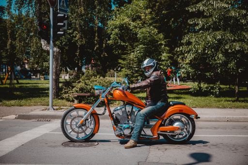 A biker with a helmet on a beautiful orange motorcycle on the road with green trees in the background