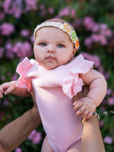 A newborn baby girl with pink knitted clothes and a head accessory in woman's arms