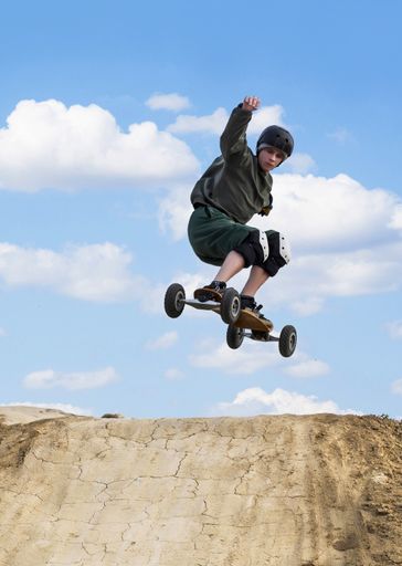 A vertical shot of a young skateboarder jumping over a hill in a skateboard park