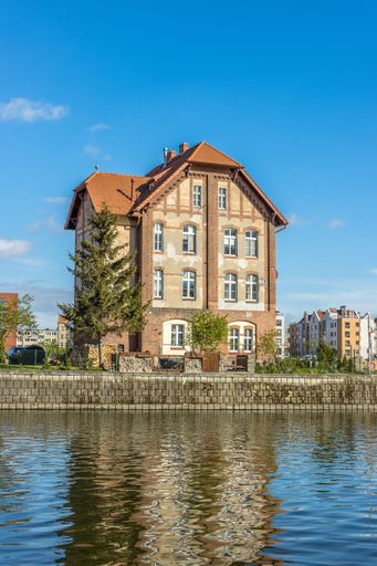 A vertical shot of an old residential building reflected on the water under the blue sky in Gdansk, Poland