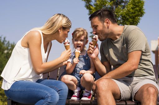 A selective focus shot of a young happy family eating ice cream with their daughter