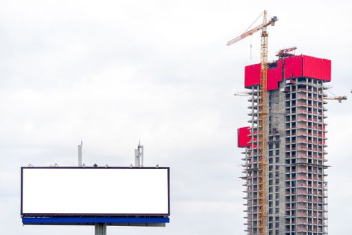 A crane next to an unfinished building with a blank billboard with copy space