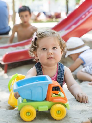 A vertical shot of Caucasian kid playing with toys on sandy playground