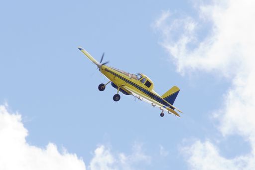 A low-angle shot of a yellow firefighting plane flying in the blue cloudy sky