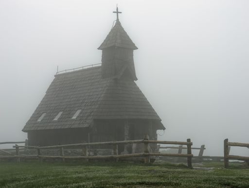 Wooden tower with the cross of the Church of the Mary of the snows on foggy day, Velika Planina, Slovenia