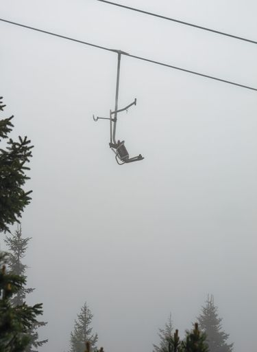 A vertical shot of a cable car above the pine trees on a foggy day, Velika Planina, Slovenia. Travel destination for family hiking.