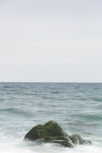 A vertical shot of the rocks in the middle of the ocean captured on a cloudy day
