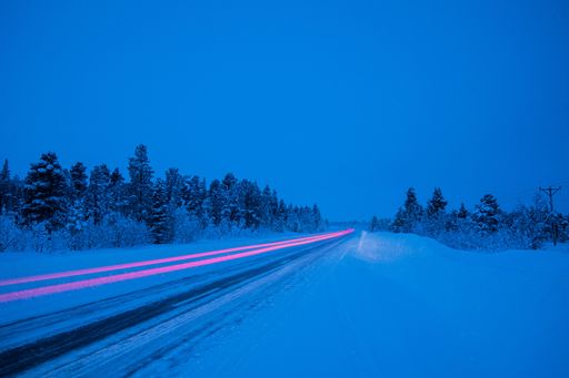 A long exposure of snow covered road with red light surrounded by trees in evening