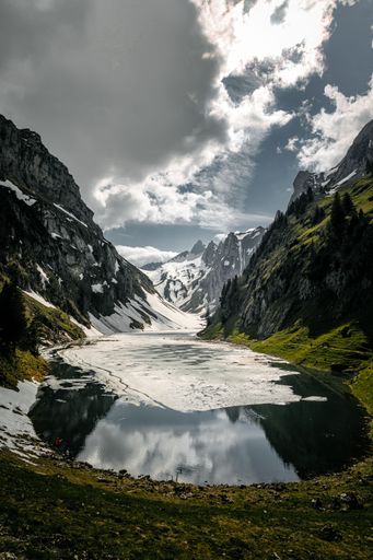 A vertical shot of a small lake surrounded by rocky mountains in a rural area in winter