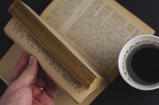 A high angle shot of a cup of coffee and an open book on the table