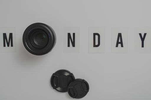 A top view of a white surface with Monday spelling and a camera lens replacing the letter o