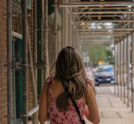 A back shot of a young girl walking through building construction  with a blurry street background