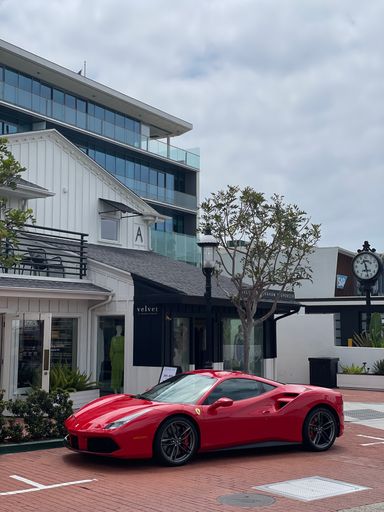 A vertical shot of an awesome Red Ferrari 488 in Newport Beach near the building on a cloudy day