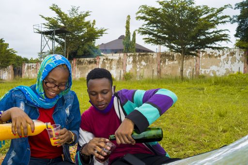 A happy Nigerian couple drinking juice and enjoying their picnic on a grass-covered meadow