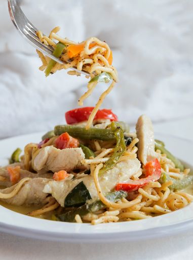 A vertical shot of a plate of delicious vegetable and chicken noodles on a white surface