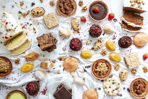 A high angle shot of delicious cakes, cupcakes, muffins, sweets, and chocolates on a white surface