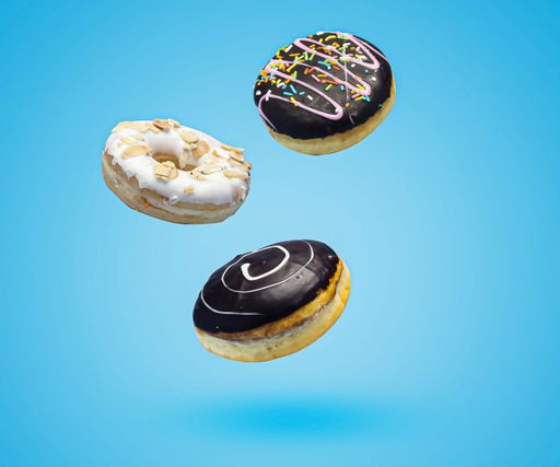Dark chocolate and vanilla sweet donuts with sprinkles flying over blue background