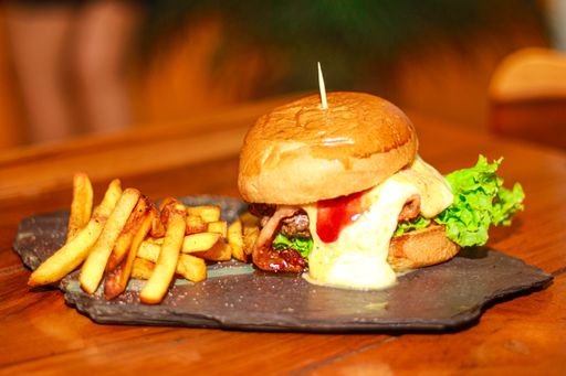 A selective focus shot of a black dish with a delicious hamburger and french fries on a wooden surface