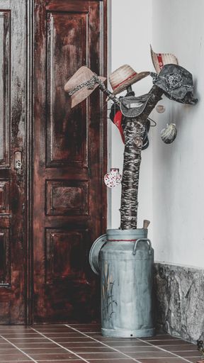 A vertical shot of a modern hat rack with a metal milk keg as a leg and several hats hanging from it
