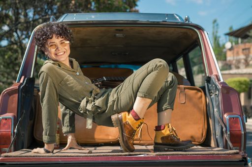 A curly stylish model laughing and posing for a photshot on the back of a car on a bright sunny day
