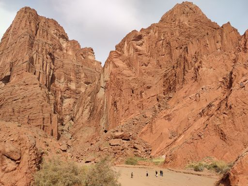 A dry landscape of red rock formations against a blue cloudy sky