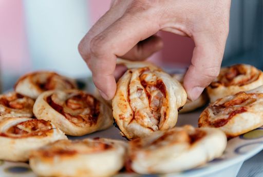A closeup shot of a hand grabbing a mini pizza bagel on a plate