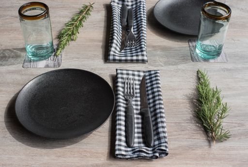 A closeup shot of black plates with napkins, fork and knife, glass cups and fir tree leaves