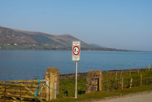 An All Dogs must be kept on a lead sign on a post in the coastal Omeath village, with mountains and water in the background
