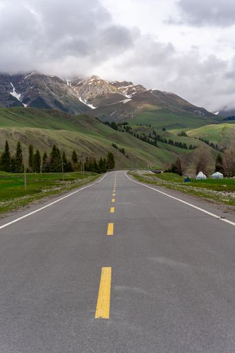 A vertical shot of an empty road with mountains in the background under a cloudy sky