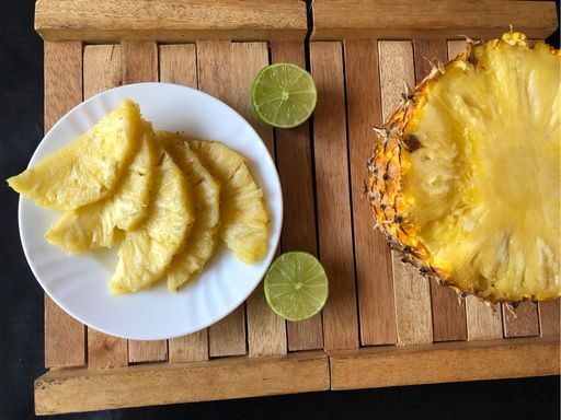 A high angle shot of fresh pineapple with lime on a wooden tray
