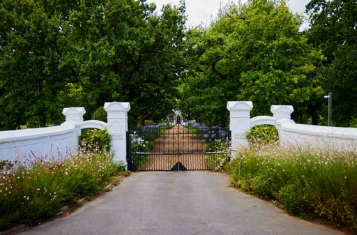 The beautiful white fenced decorative metal entrance of a garden on a sunny day
