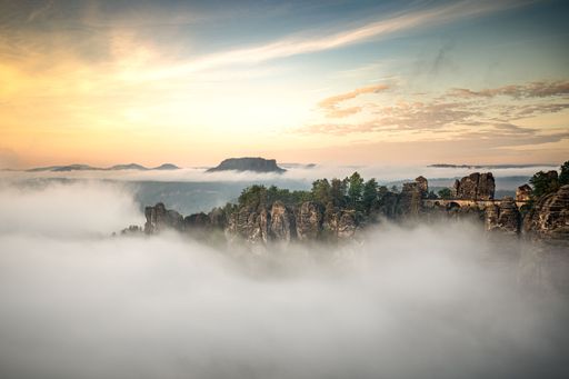 The beautiful scenic view of the rocky mountain top covered in fog under the sunrise sky with clouds