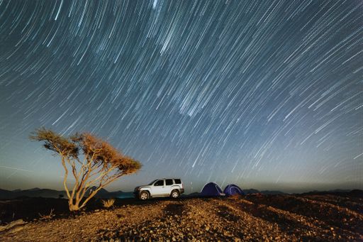 An off-road car and tents on a hill under a starry night with long exposure